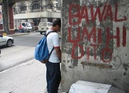 Man urinating beside a bawal umihi dito sign in the Philippines