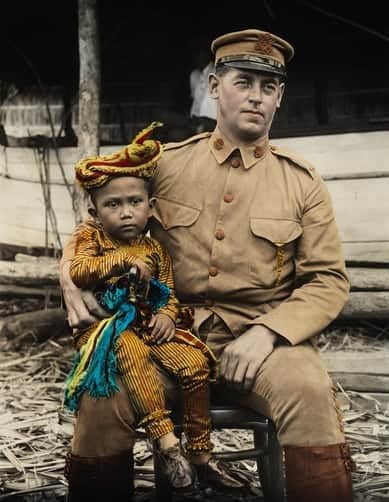 A young Moro boy sits on the knee of an American lieutenant